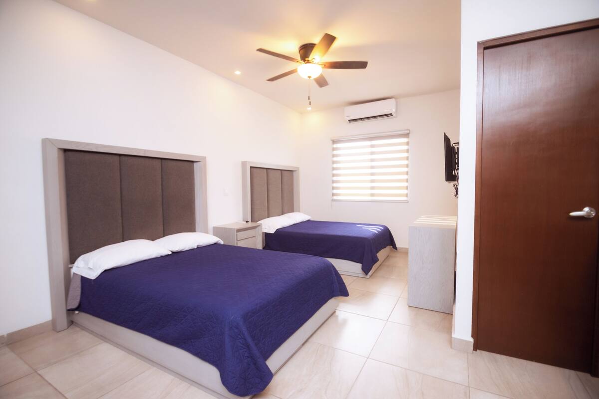 A hotel room with two beds, a ceiling fan, an air conditioning unit, and a door.