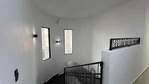 Una scala con ringhiera in metallo nero, un muro bianco e due finestre con cornici nere.
