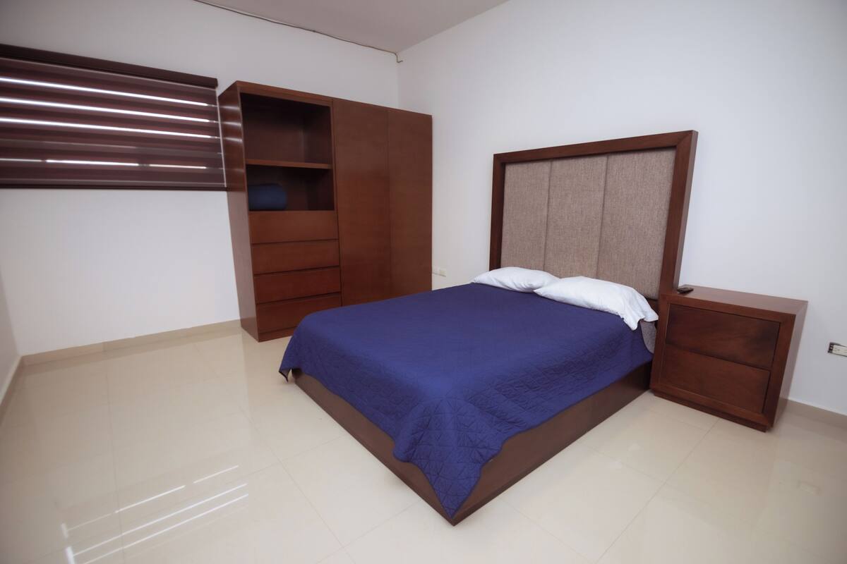 A bedroom with a bed, a nightstand, a wardrobe, and a window with blinds.