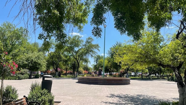Una piazza aperta con un monumento circolare, panchine e alberi.