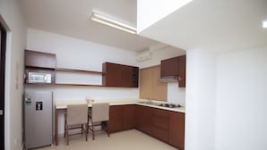 Una cucina compatta con frigorifero, microonde e fornello. Sono presenti due sedie e un piccolo tavolo.
