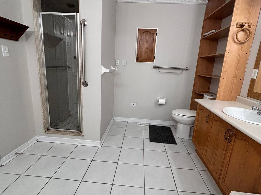 A bathroom with a shower, toilet, sink, and wooden shelving.