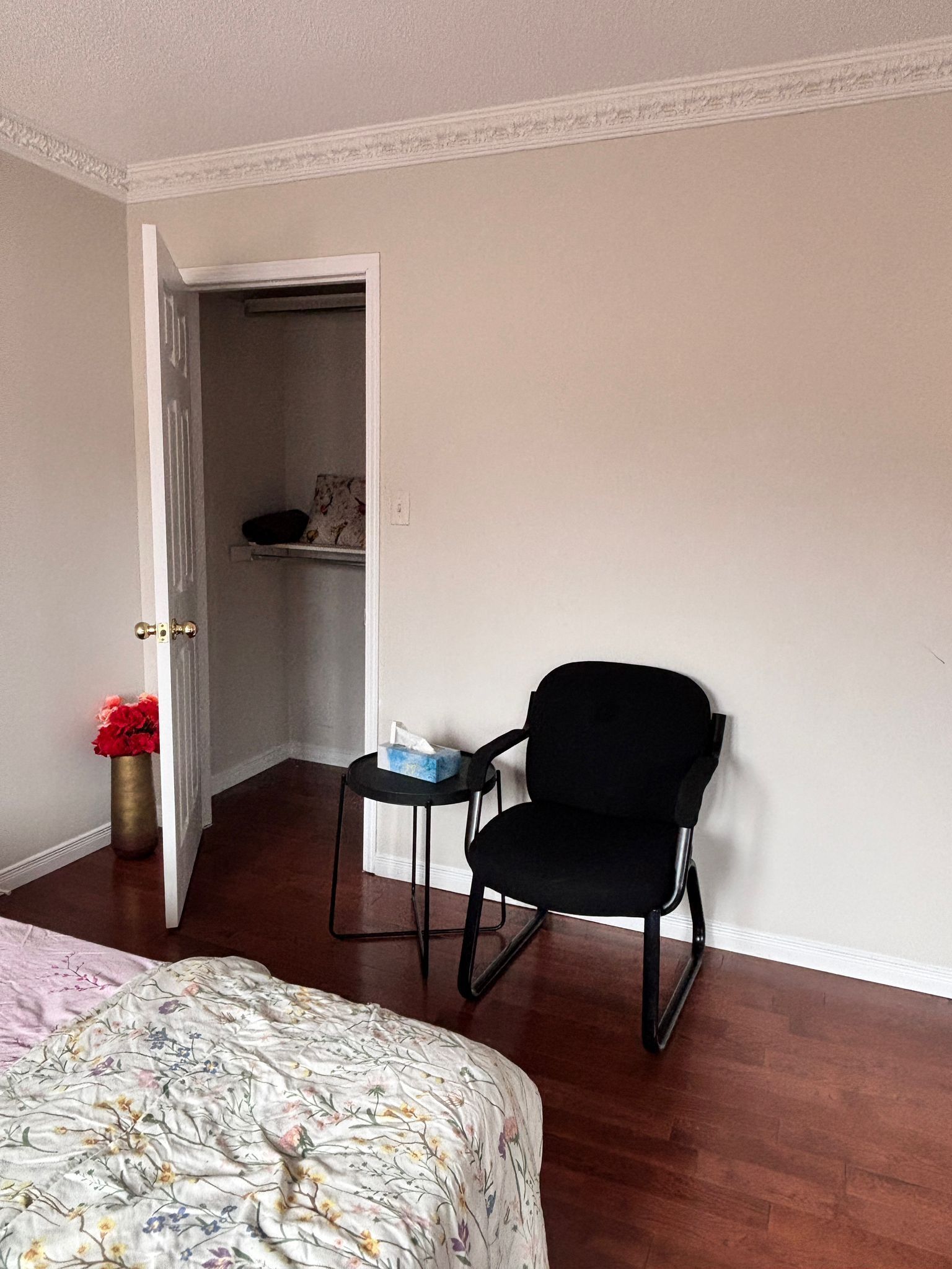 A bedroom with a bed, a black chair, a small table with a tissue box, and a closet with a shelf.