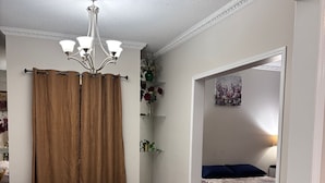 A room with a bed, a chair, a small table, a shelf with plants, and a painting on the wall. - Beautiful Queen Room (Brampton)