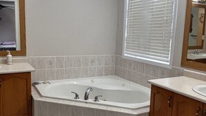 A bathroom with a freestanding bathtub, a vanity with a sink, and a window with blinds. - Beautiful Queen Room (Brampton)