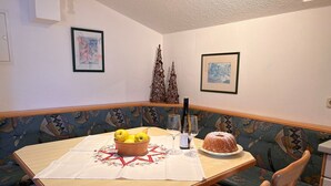 Un comedor con una mesa lista para dos personas, con un frutero, copas de vino y un pastel bundt. La habitación tiene un banco estampado y dos cuadros en la pared.