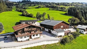 Un edificio grande y moderno con techo plano, rodeado de campos verdes y árboles frondosos.