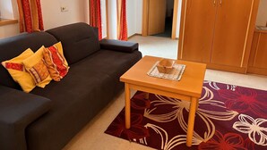 Una sala de estar con un sofá oscuro, una mesa de madera con un adorno y una alfombra roja con motivos florales.