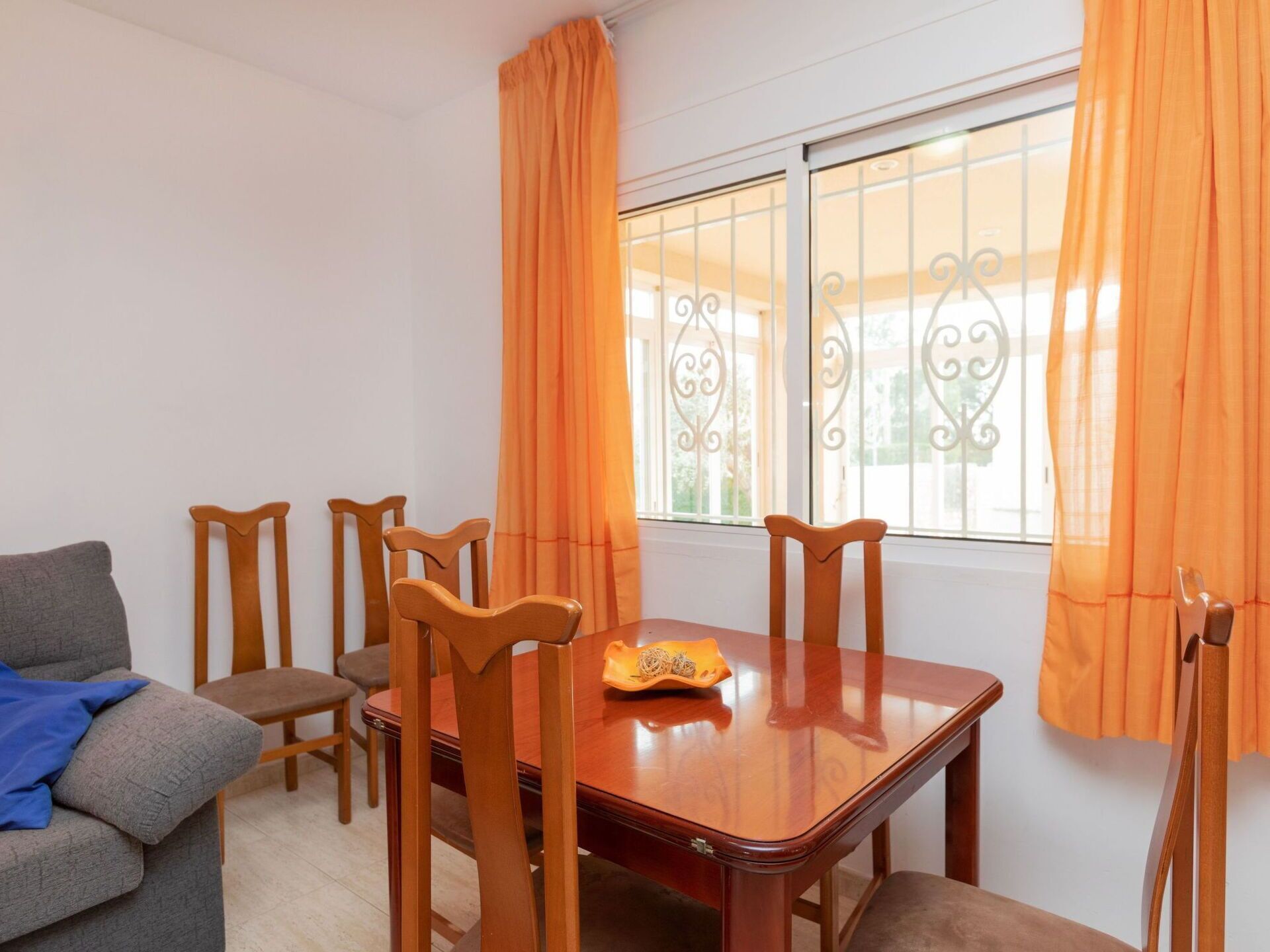 Un coin repas avec une table et des chaises en bois, un canapé gris et des rideaux orange.
