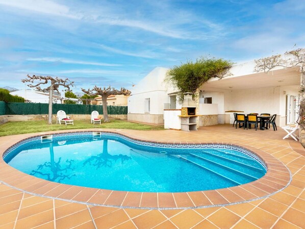 Una piscina con borde de azulejos, zona de barbacoa y mobiliario exterior.