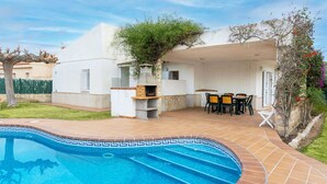 A swimming pool with a tiled edge, a barbecue area with a table and chairs, and a white building with a flat roof. - Stunning private villa for 6 guests with private pool, A/C, TV, patio and pets allowed (L'almadrava)