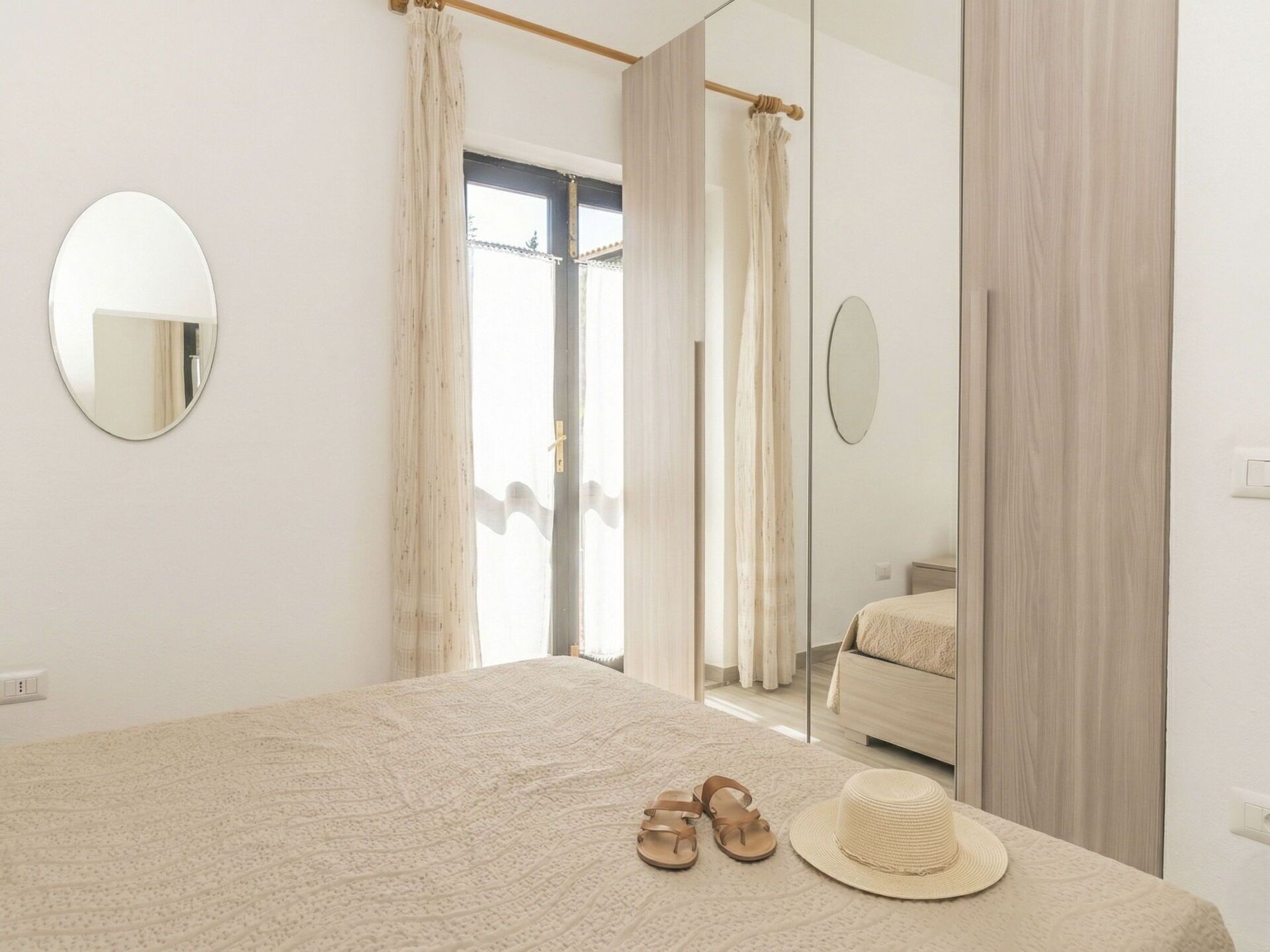 Een slaapkamer met een bed, een spiegel, een kledingkast en een deur naar een andere kamer.