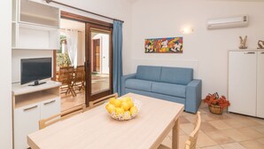 Un espace de vie compact comprenant un coin repas, un canapé, un téléviseur et un tableau au mur.