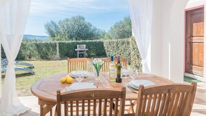 Une terrasse extérieure avec une table en bois dressée pour le repas, entourée de rideaux blancs.