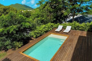 A rectangular pool with two lounge chairs on a wooden deck, surrounded by lush greenery and a mountain in the background. - 2 rooms with private pool | Villa 2 (Pigeon-Pea Hill)