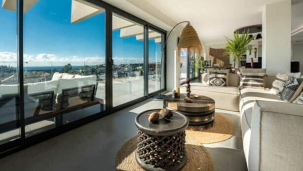 A modern living room with large windows, a sofa set, a coffee table, and a decorative lamp. - Apartment in Estepona - Boho Chic - Ojala Casa (Estepona)
