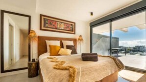 A modern bedroom with a large bed, a view of the city, and a balcony. - Apartment in Estepona - Boho Chic - Ojala Casa (Estepona)