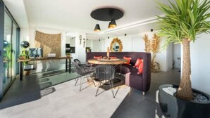 A modern living space with a dining area, a sofa, and a large plant. - Apartment in Estepona - Boho Chic - Ojala Casa (Estepona)