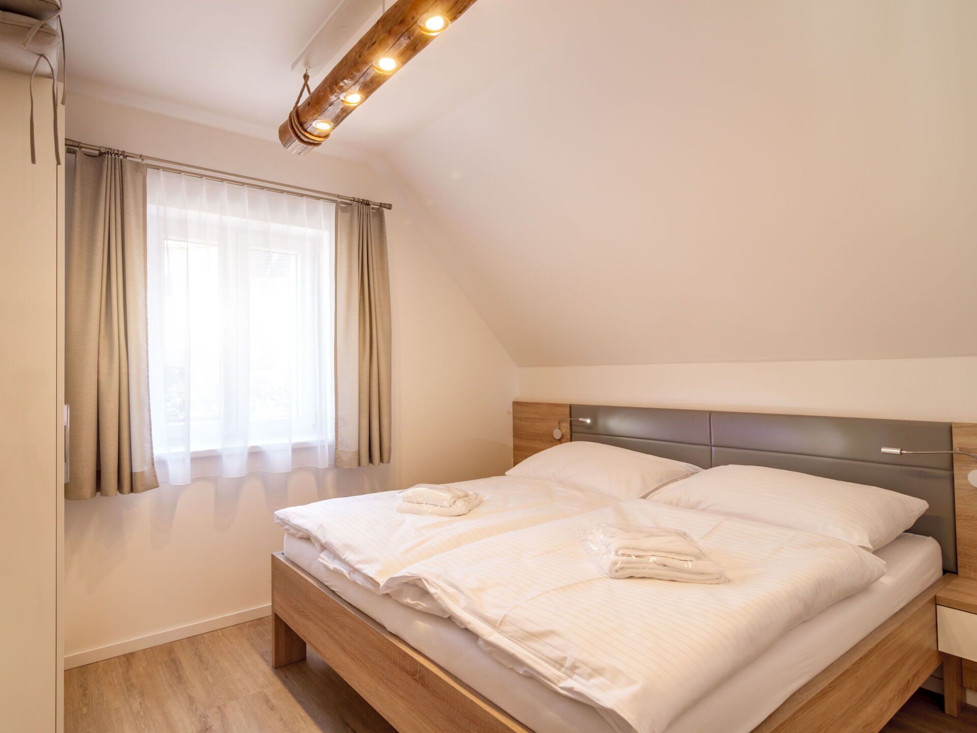 A bedroom with a wooden bed, a nightstand, a window with curtains, and a ceiling light fixture.