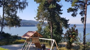 A wooden playhouse with a swing set in a natural setting with trees and a lake in the background. - Beautiful private villa for 9 people with WIFI, TV, terrace and pets allowed (Lojzova Paseka)