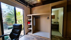 A room with a black leather chair, a wooden floor, a built-in shelf unit, and a view of palm trees outside.