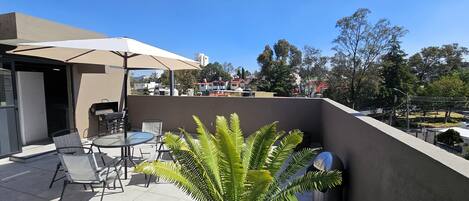 A rooftop patio with a table, chairs, a grill, and a large umbrella.