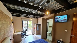 A bedroom with a bed, a chair, a TV, and a bathroom visible through an open door.