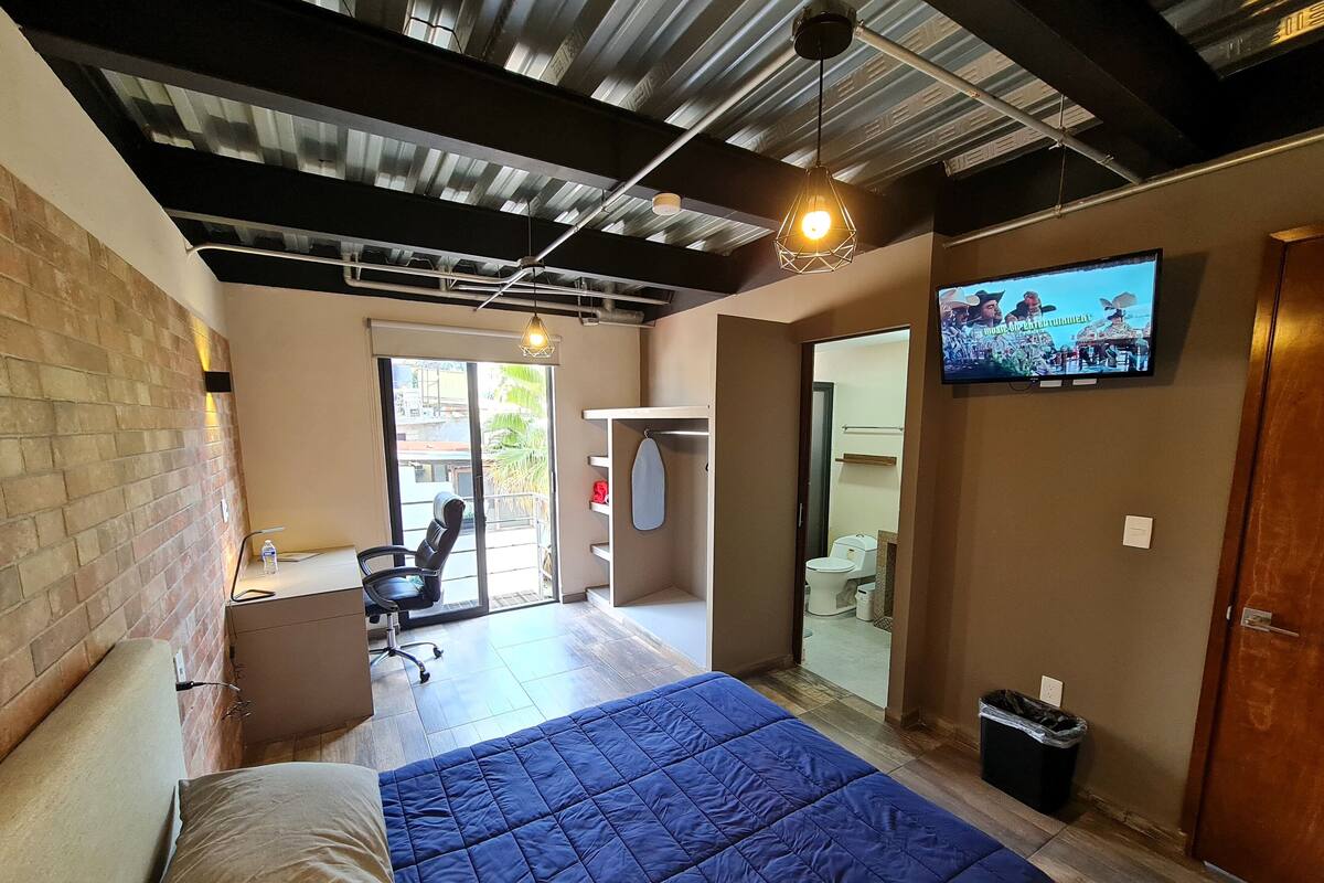 A bedroom with a bed, a chair, a TV, and a bathroom visible through an open door.