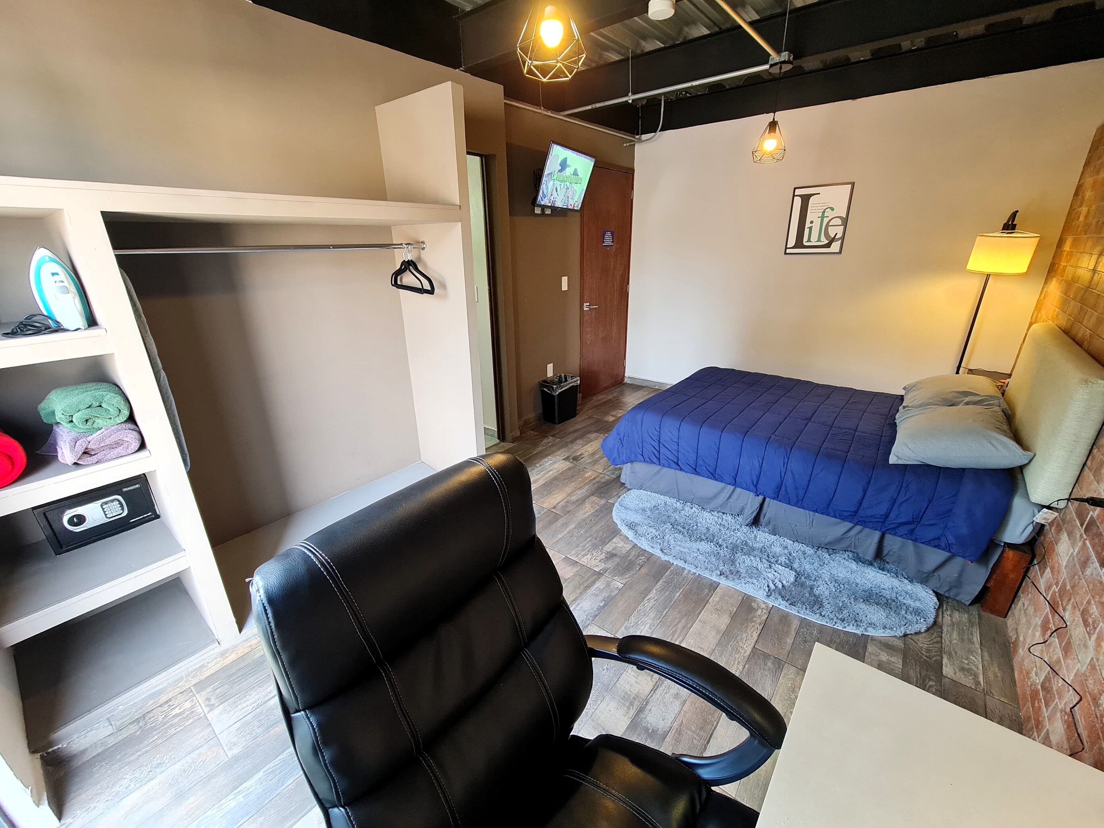 A compact hotel room with a bed, a desk, a chair, a wardrobe, and a television.