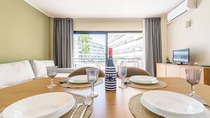 A hotel room with a dining table set for four, a minibar, a television, and a view of the outside balcony.