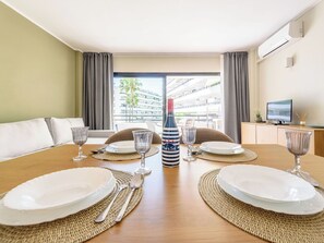 A hotel room with a dining table set for four, a minibar, a television, and a view of the outside balcony.