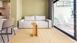 A modern room with a sofa, a small round table with a teapot and cup, a chair, and a view of the outside.
