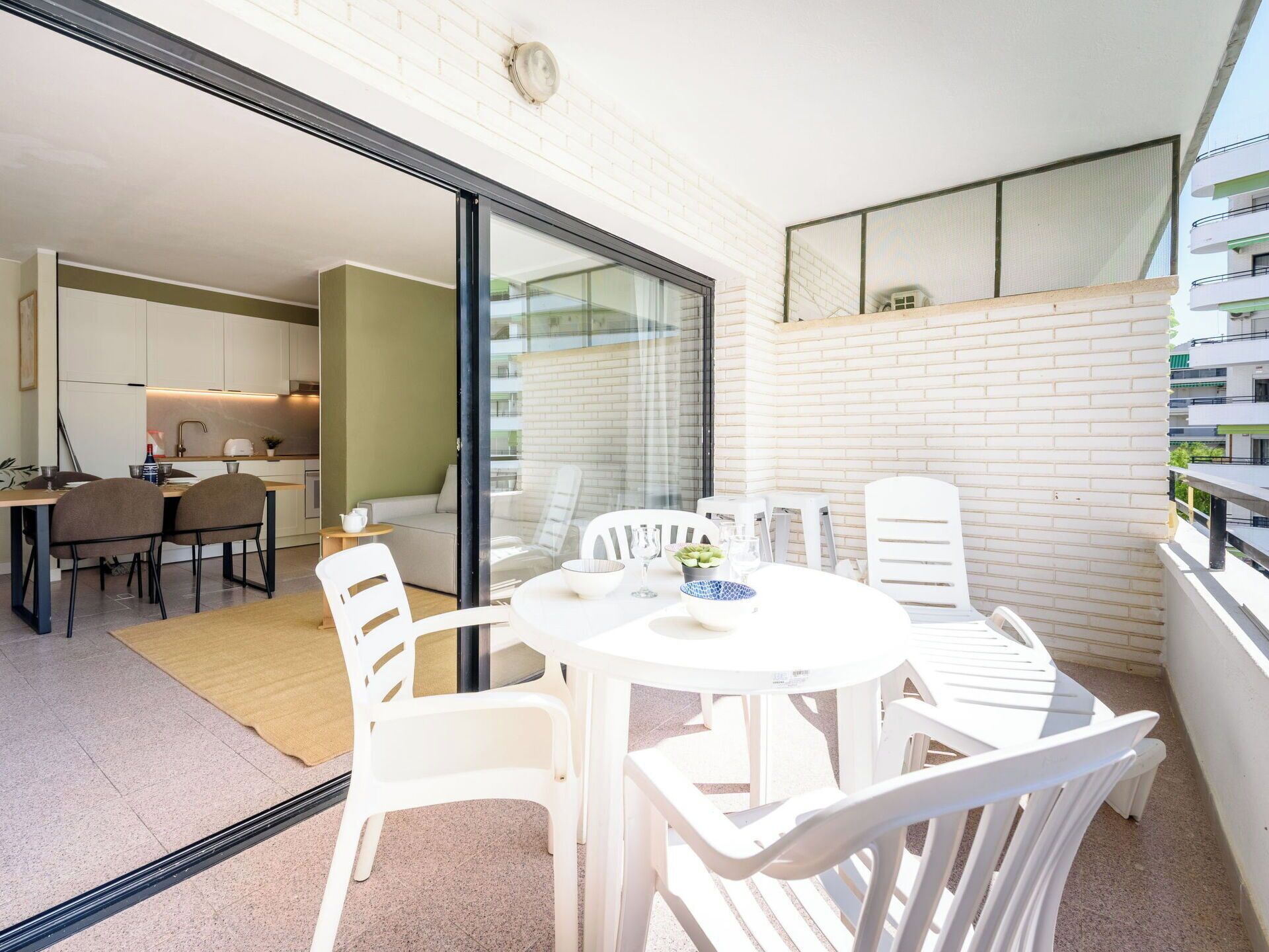Un balcon avec une table et des chaises, un coin cuisine et une vue sur un immeuble.