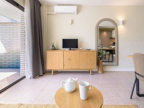 A modern living room with a wooden cabinet, a flat-screen TV, a dining area with a table and chairs, and a large mirror.