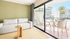 A modern living room with a sofa, a small round table, and a view of a balcony with outdoor furniture.