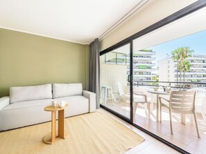 A modern living room with a sofa, a small round table, and a view of a balcony with outdoor furniture.