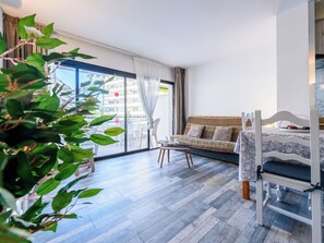 A room with a bed, a sofa, a dining table, and a balcony with a view of buildings.