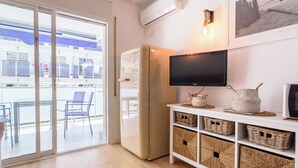 A modern living room with a sliding glass door leading to an outdoor area, a flat-screen TV mounted on the wall, and a white cabinet with wicker baskets.