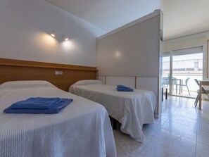 A hotel room with two beds, a wooden headboard, a balcony with a table and chairs, and a view of the sea. - Cosy apartment for 3 people with A/C, WIFI, pool and terrace (Salou)