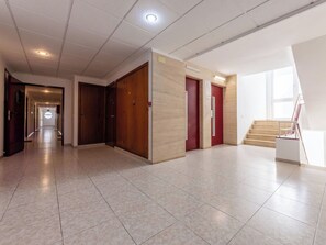 Un pasillo espacioso con piso de baldosas, puertas de madera y una escalera que sube a un nivel superior.