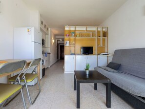 A compact living space with a kitchenette, a sofa, a dining table with chairs, and a TV on a wooden cabinet.