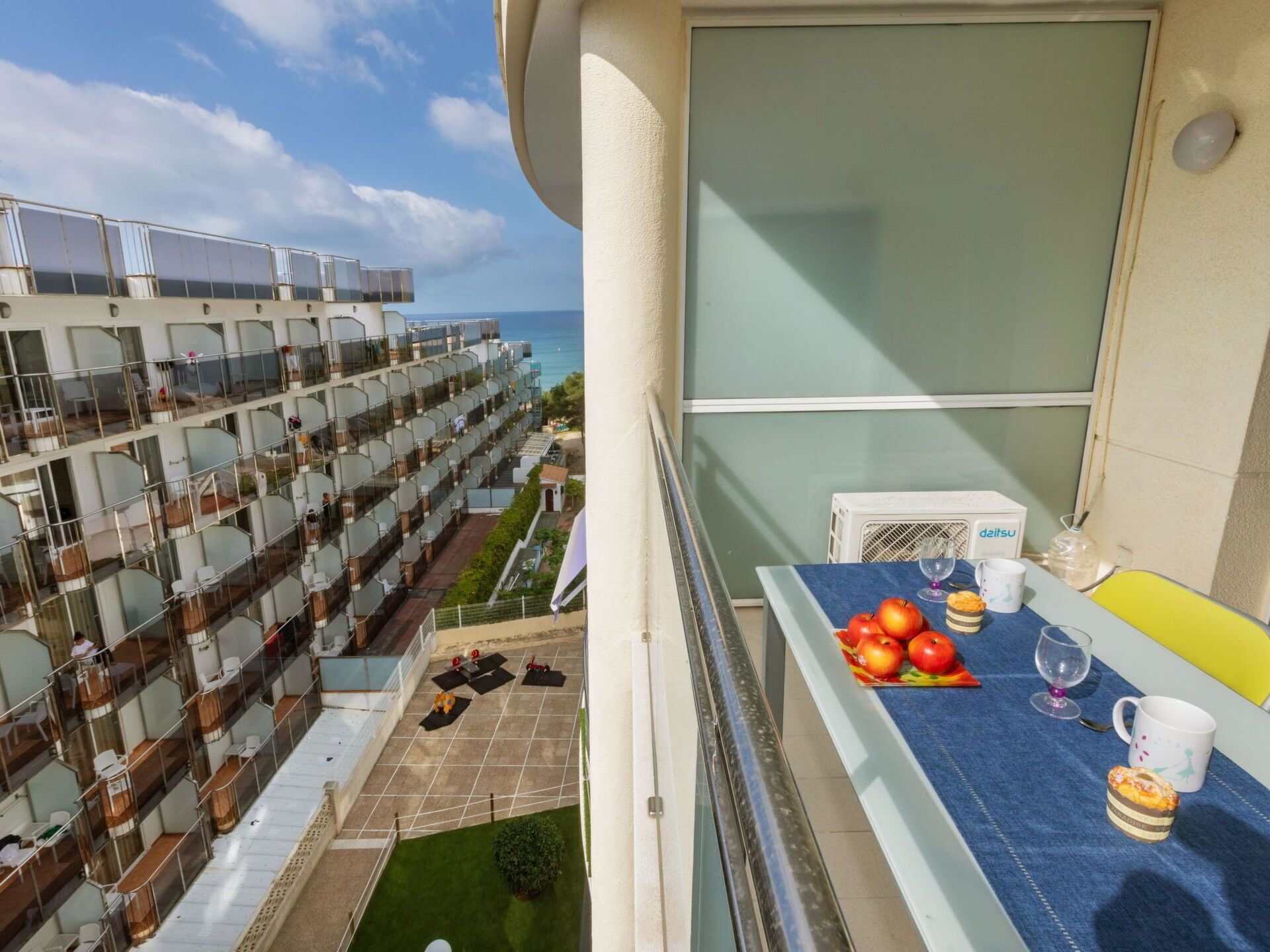 A balcony with a table set for breakfast, including apples, a glass, and a muffin.