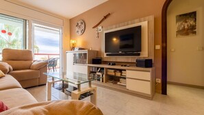 Una sala de estar con sofá, una mesa de centro de vidrio, televisor y estantería.