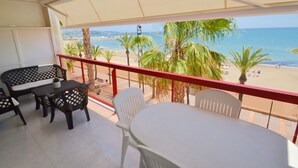 Un balcón con mesa y sillas, con vistas a una playa con palmeras y el mar.