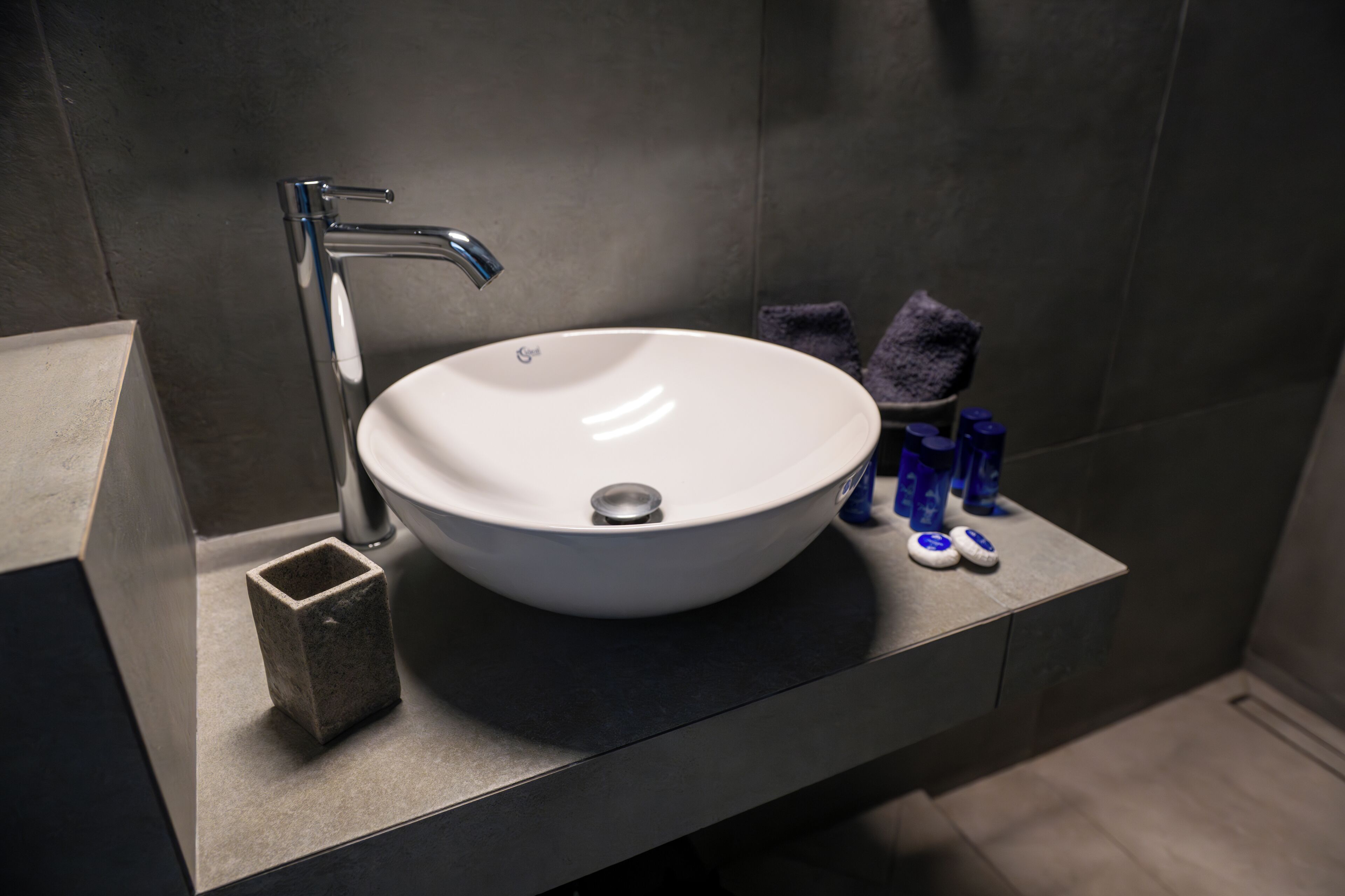 Ein modernes Badezimmer mit einem weißen Waschbecken, einem chromfarbenen Wasserhahn und einem kleinen Steingefäß.