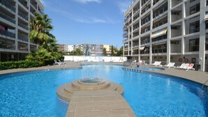 Une piscine entourée d’un immeuble à plusieurs étages doté de balcons, de palmiers et surplombant un ciel dégagé.