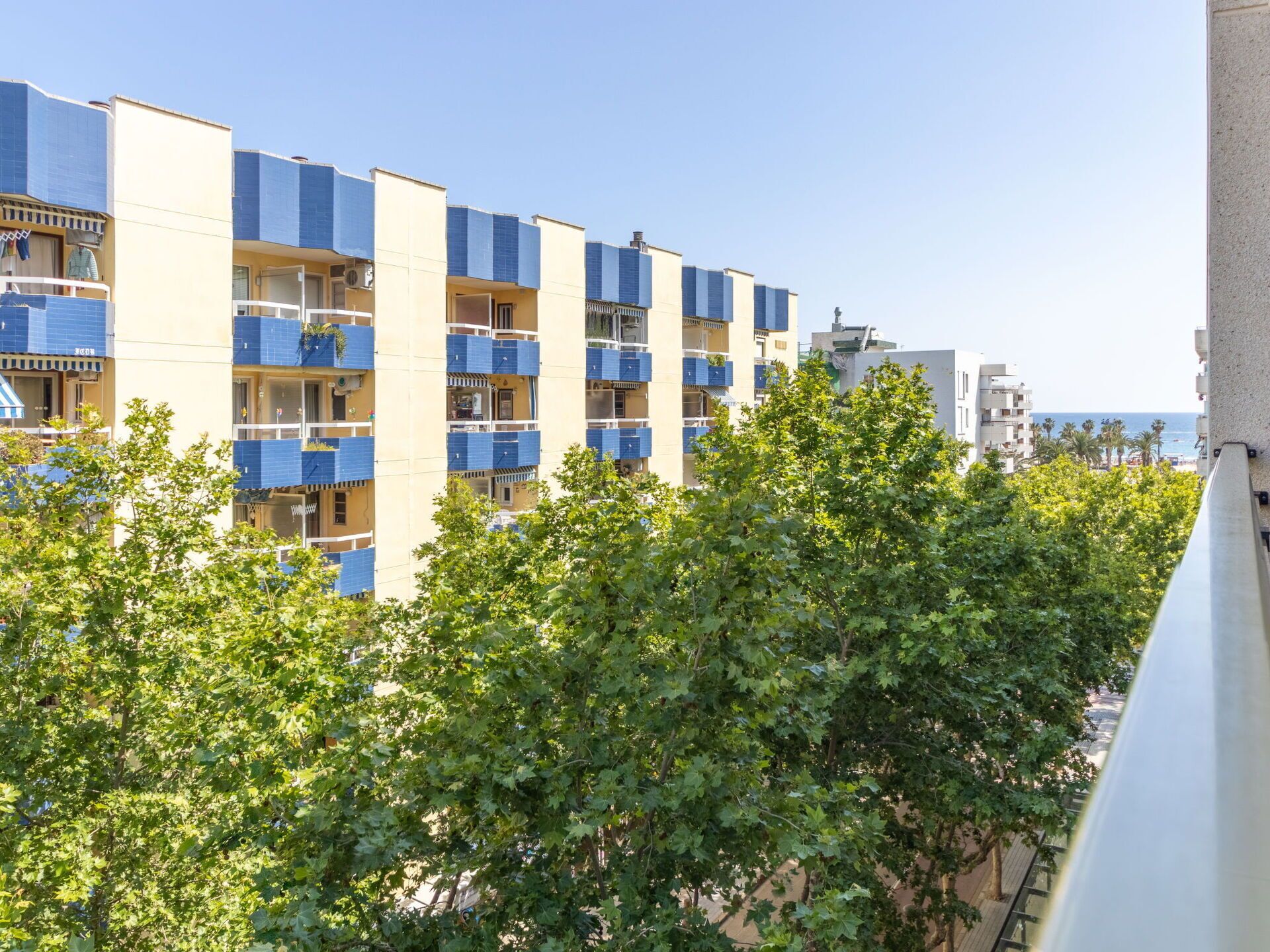 Un hotel de varios pisos con balcones, vista al mar y exuberante vegetación en primer plano.