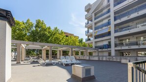 Een terras op het dak met lounge stoelen en een overdekte zithoek, omgeven door een meerlaags gebouw met balkons.