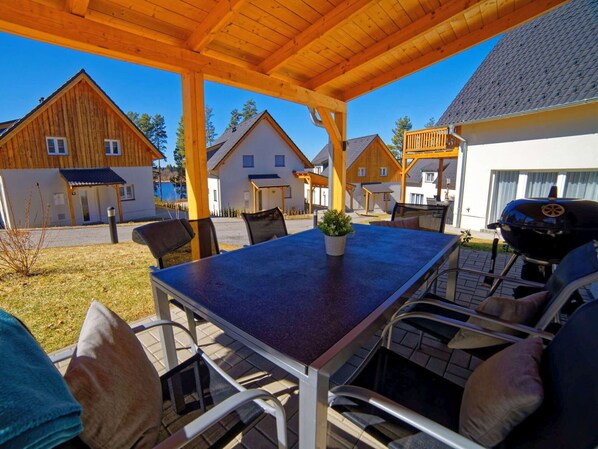 An outdoor patio with a table and chairs, a grill, and wooden houses in the background. - Wonderful private villa for 10 people with WIFI, TV and terrace (Lojzova Paseka)