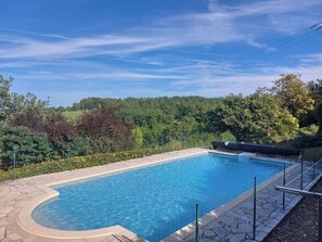 A rectangular swimming pool with a curved edge, surrounded by a stone deck and a metal fence. - Maison Privée au Calme (Campagnac-lès-Quercy)